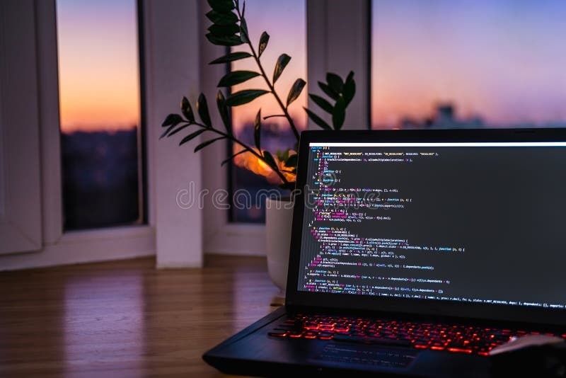 Bärbar dator med programmeringskod vid ett fönster i skymningen